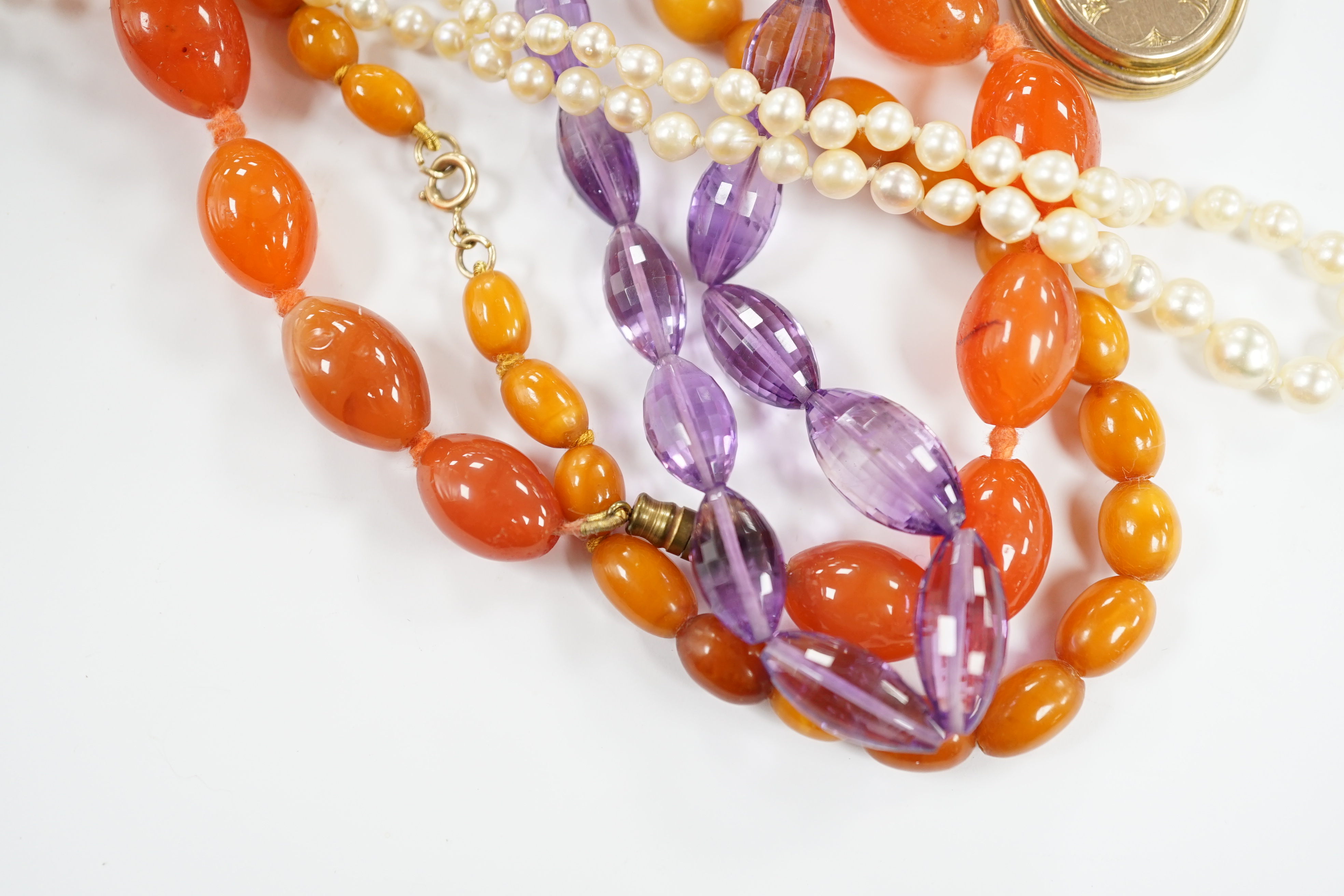 A gold plated oval locket and four assorted single strand necklaces including cultured pearl, amber, agate and amethyst.